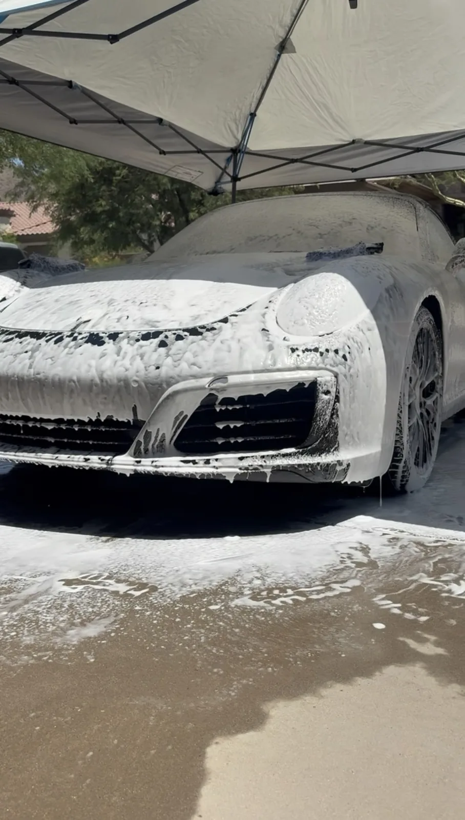 Porsche 911 covered in foam during a pre-wash under a shade canopy